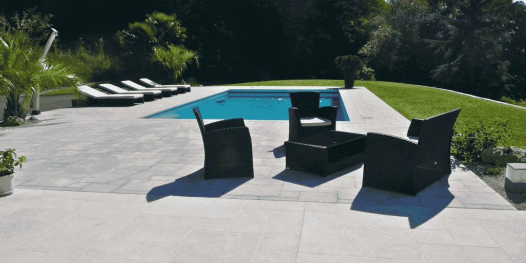 Terrasse de piscine en carrelage pierre claire avec salon de jardin à Pau